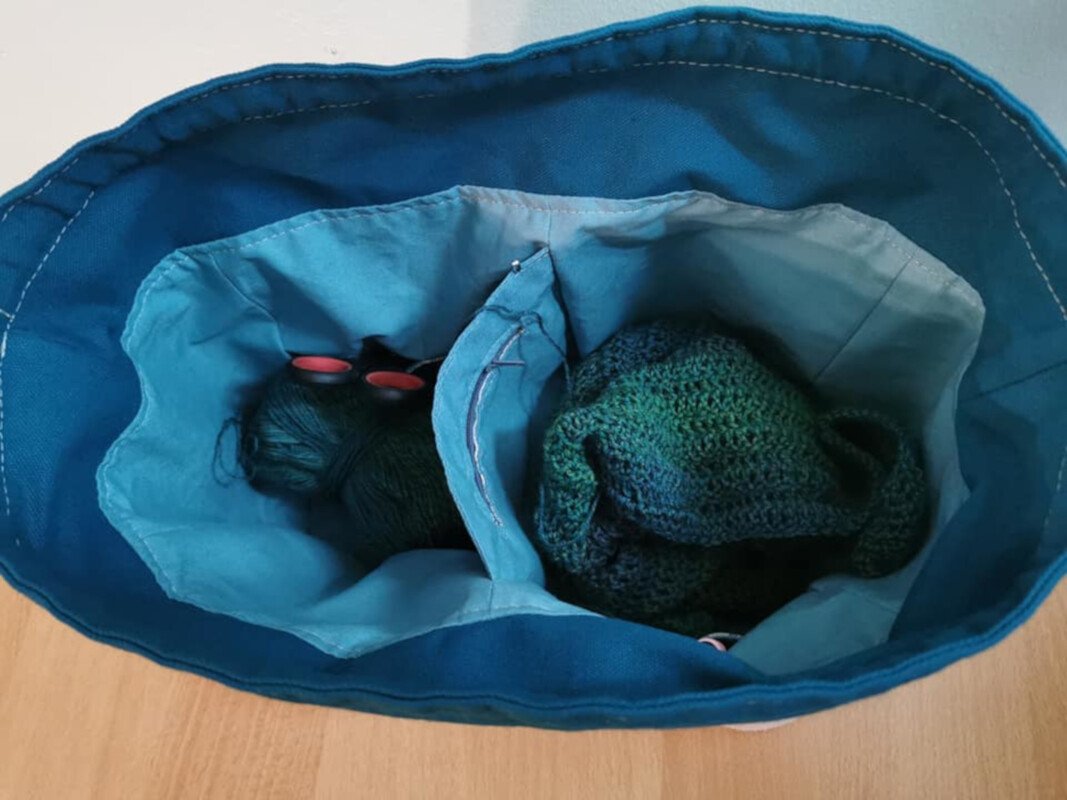 Dunkelblaue Utensilo-Tasche mit hellblauem Innenfutter und zwei Fächern, gefüllt mit Garn und begonnenem Häkelstück.