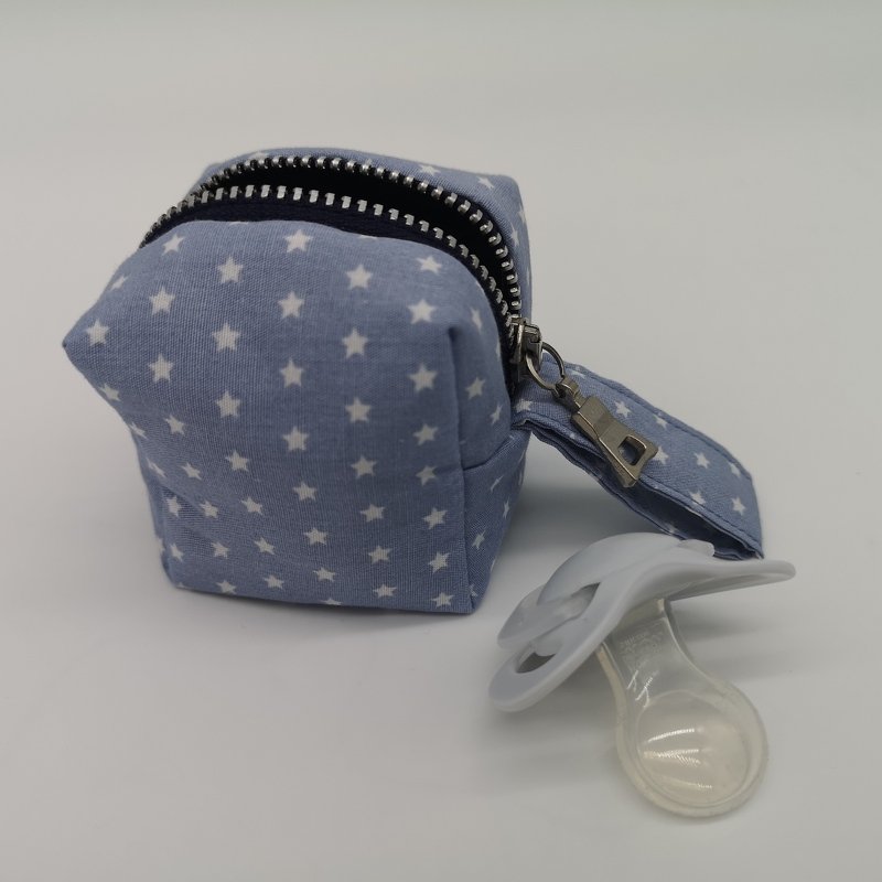 Hellblaues Täschchen mit weißen Sternen, Reißverschluss und Metallclip; weißer Schnuller daneben
