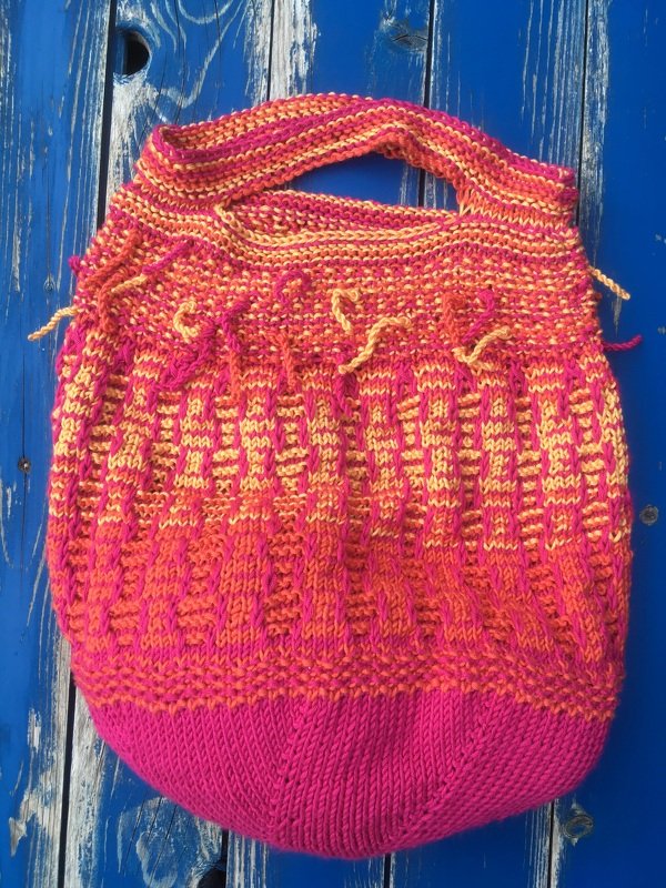 Gestrickte Tasche in Pink und Orange auf blauem Holzuntergrund