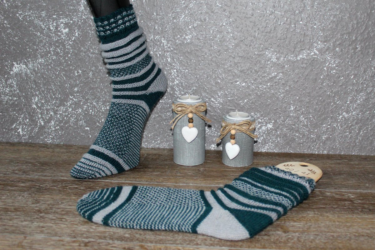 Gestrickte grün-graue Streifensocke an Schaufensterbein und zweite Socke auf Sockenspanner vor Kerzenhaltern