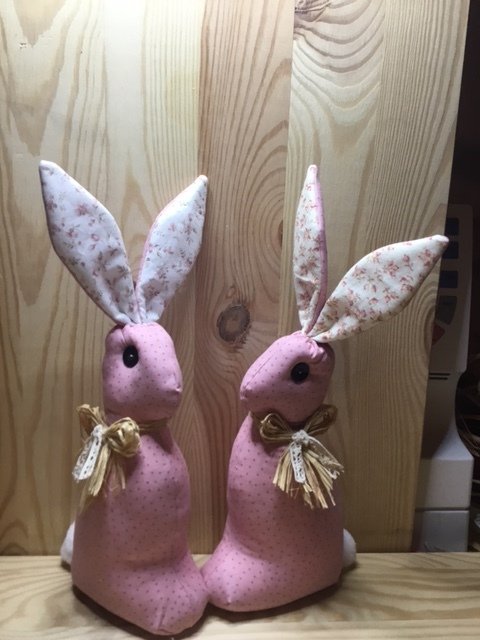 Zwei rosa Stoffhasen mit gepunktetem Stoff, geblümten Innenohren und Bastschleifen vor einer Holzplatte