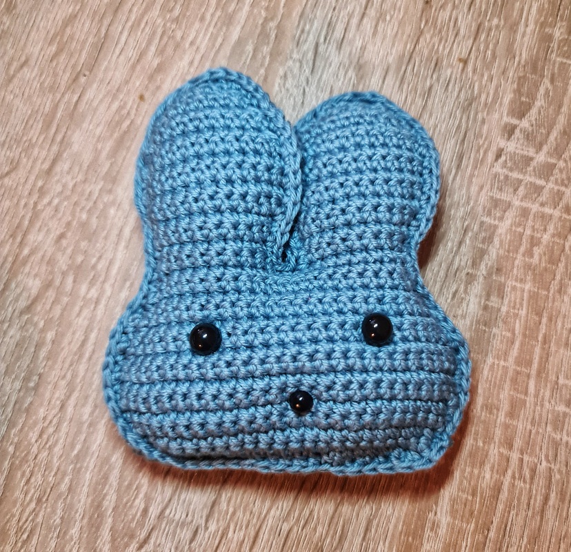 Gehäkelter blauer Hasenkopf mit schwarzen Augen auf Holzuntergrund