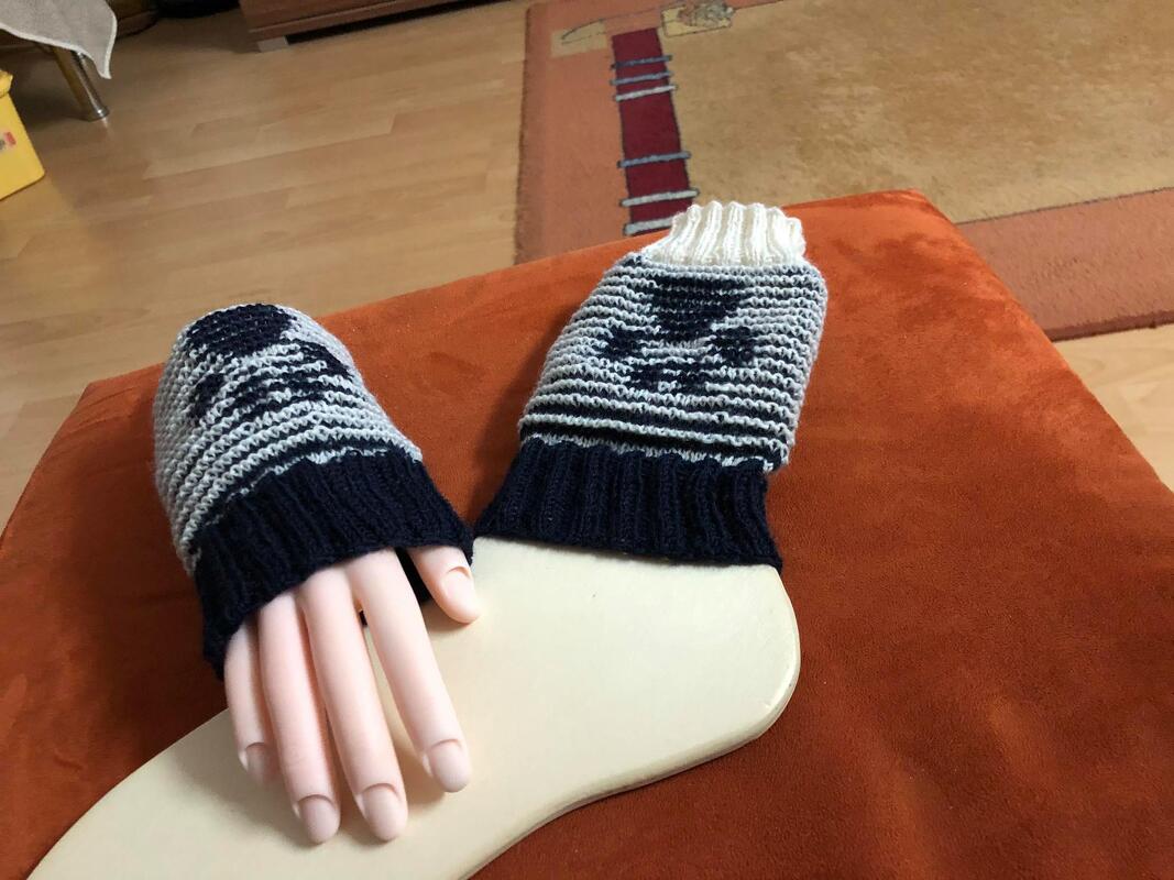 Zwei gestrickte Stulpen mit Muster in Dunkelblau, Hellgrau und Creme auf Handformen.