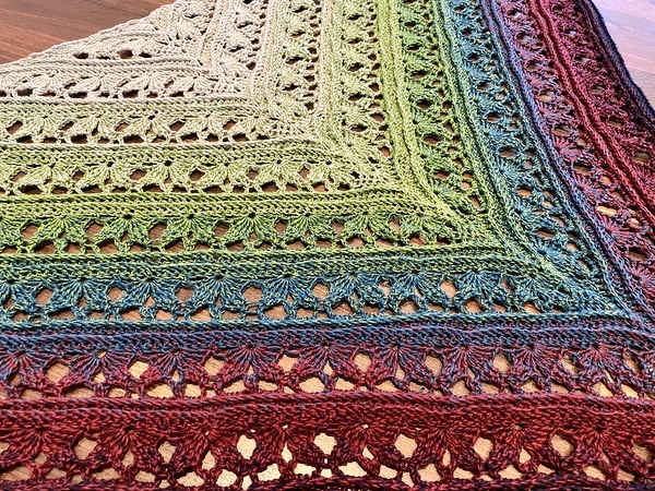 Gehäkeltes Dreieckstuch, Detailaufnahme mit Farbverlauf von Creme über Grün bis Blau und Rot sowie offenem Spitzenmuster