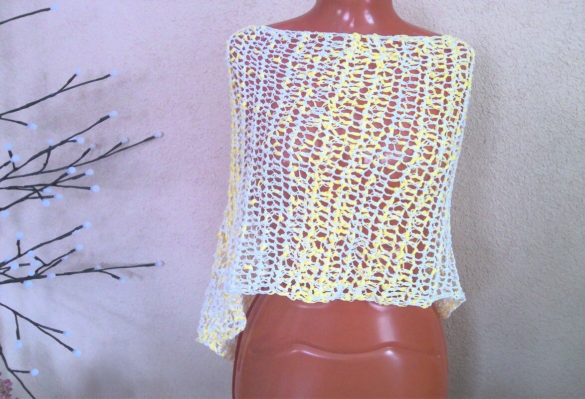 Gelb-weißer gehäkelter Damenponcho mit offenem Netzmuster auf Schaufensterpuppe
