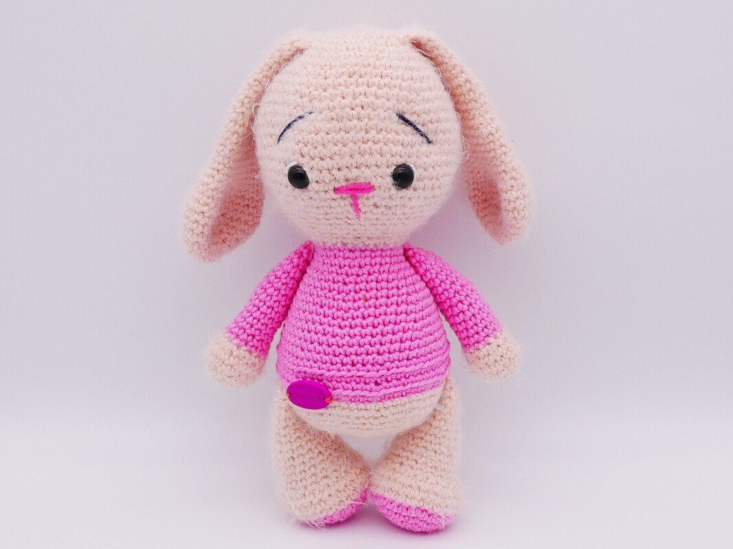 Kompakter gehäkelter Amigurumi-Hase mit langen Ohren, rosa Pullover und Knopfdetail