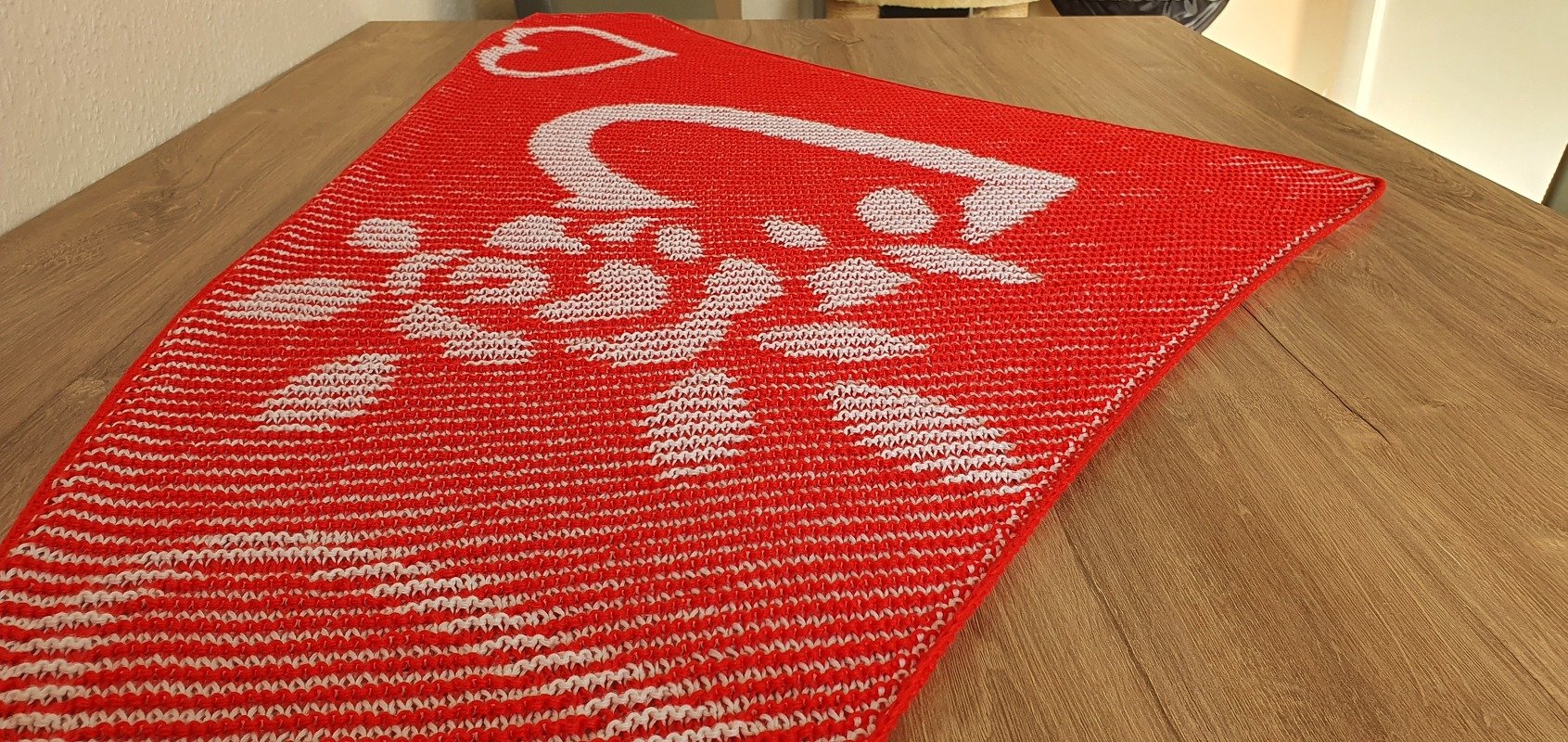 Red and white knitted shawl with heart colorwork displayed on a wooden table.