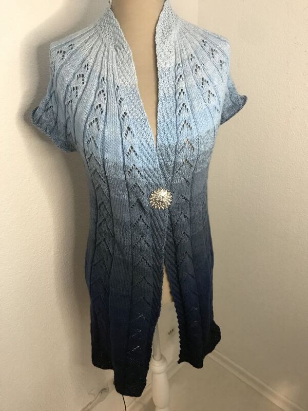 Damen-Strickweste mit blauem Farbverlauf, Ajourmuster, kurzen Ärmeln und Zierbrosche auf einer Schneiderpuppe