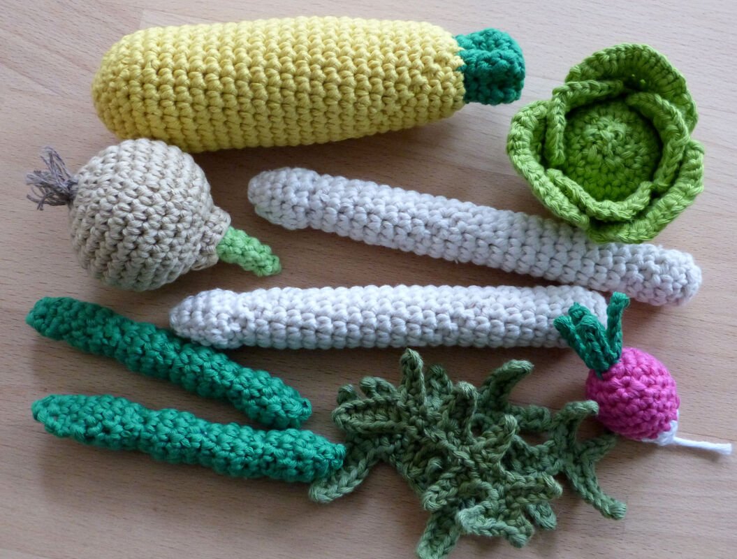 Set aus farbenfrohem gehäkeltem Gemüse (Mais, Kohl, Radieschen, Knoblauch, grüne Bohnen, Lauch) auf Holztisch.