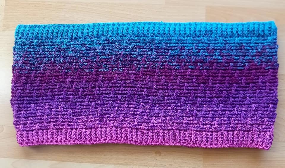 Gehäkelter Loop-Schal in Türkis, Lila und Pink, flach auf dem Tisch gelegt