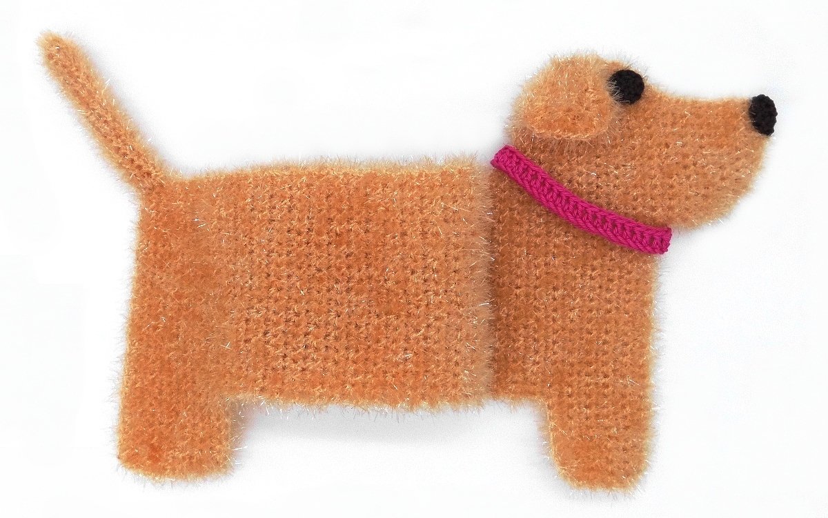 Flache gehäkelte Hunde-Applikation aus orangefarbenem Flauschgarn mit rosafarbenem Halsband und schwarzen Details