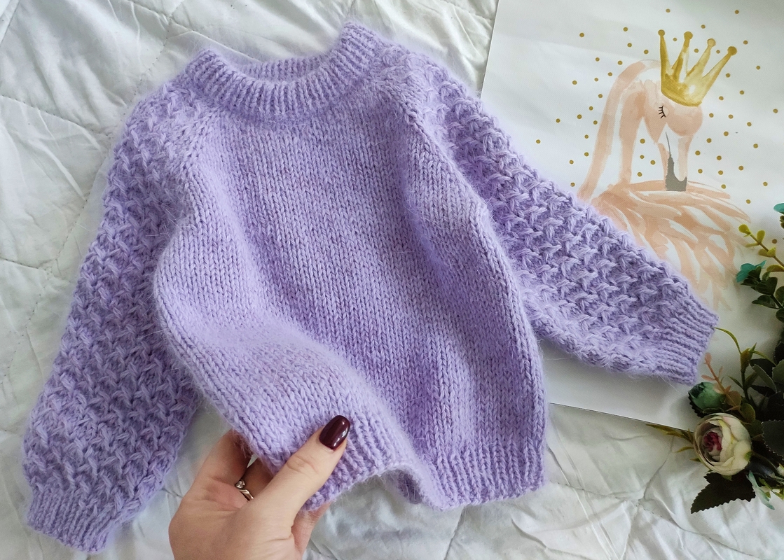 Lilafarbener Strickpullover für Kleinkinder mit glatt gestricktem Rumpf und strukturierten Ärmeln, an der Vorderkante leicht gehalten.