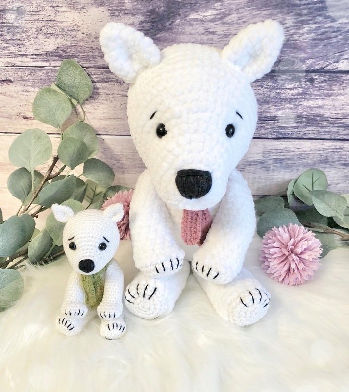 Zwei weiße gehäkelte Eisbären-Amigurumi, groß und klein, vor Holzpaneel mit Eukalyptus und rosa Blumen