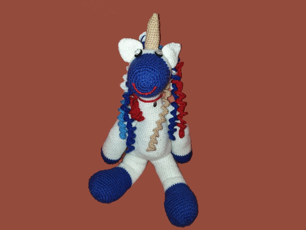 Gehäkeltes Einhorn-Amigurumi mit weißem Körper, blauem Gesicht und bunter, lockiger Mähne