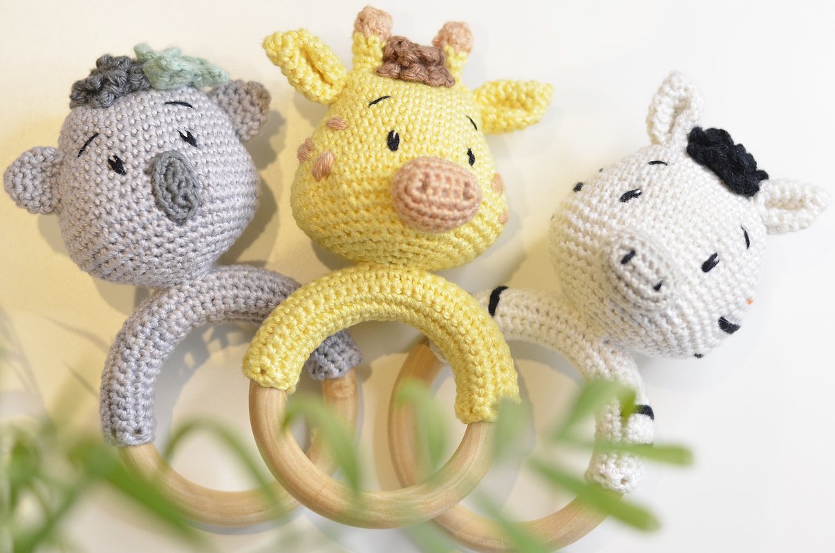 Drei gehäkelte Beißringe mit rundem Holzring: gelbe Giraffe, grauer Koala, weißes Zebra