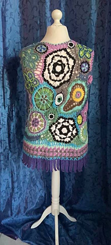 Bunte gehäkelte ärmellose Weste mit kreisförmigen und geometrischen Motiven in Lila, Türkis, Grün und Schwarz auf einer weißen Schaufensterpuppe.