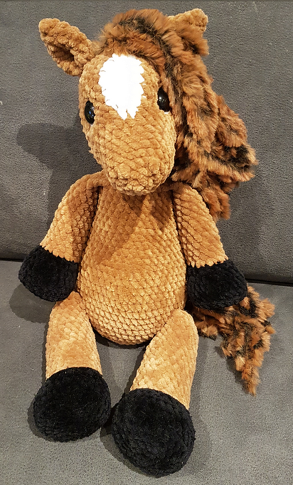 Gehäkeltes braunes Amigurumi-Pferd mit weißer Blesse und schwarzen Hufen, sitzend
