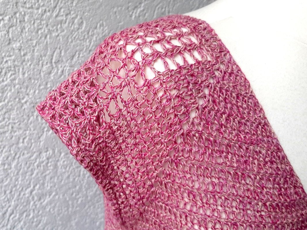 Nahaufnahme des Maschenbilds eines gehäkelten rosa Kurzarm-Shirts an der Schulter