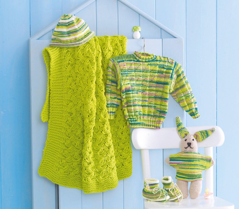 Gestrickte grüne Decke, gestreifter Pullover, Mütze, Schühchen und gestreifter Hase vor blauem Hintergrund.