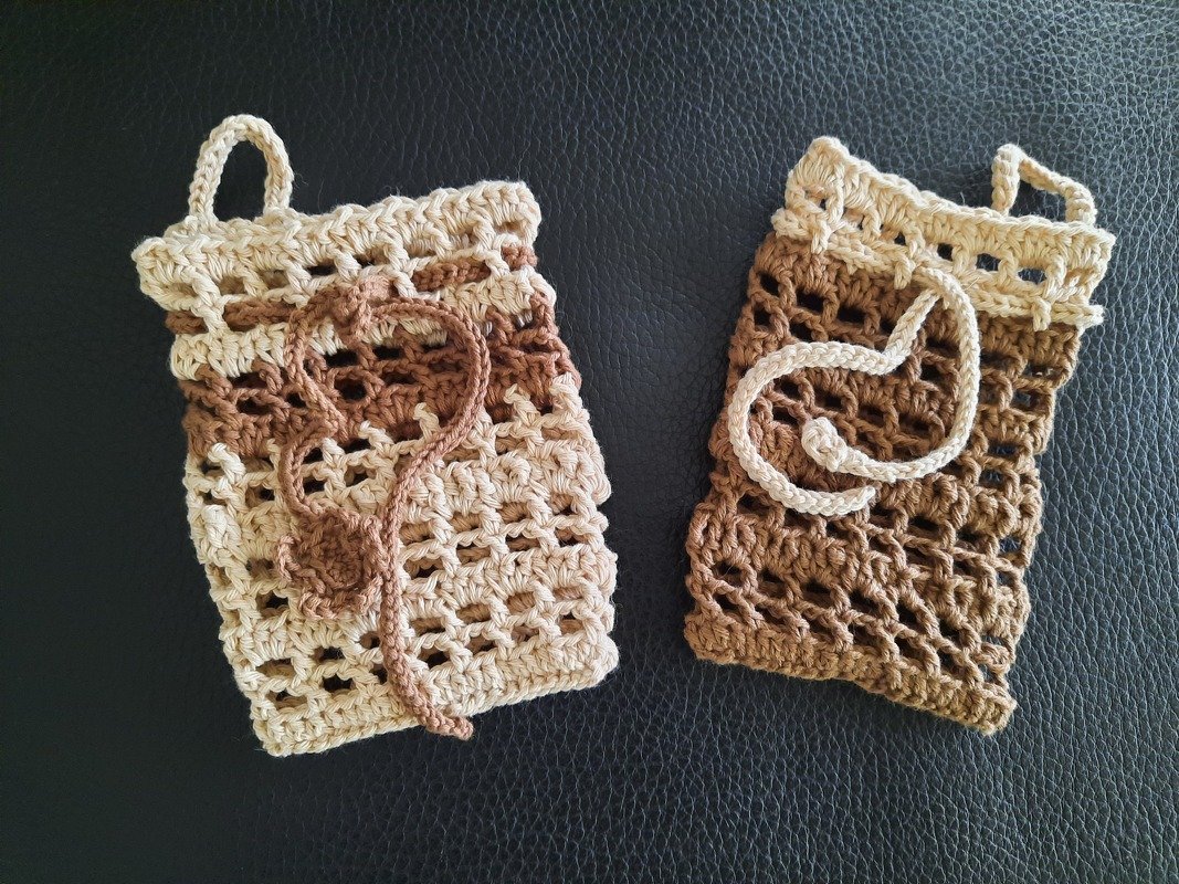 Zwei gehäkelte Netzbeutel in Beige- und Brauntönen mit Zugband auf dunklem Hintergrund