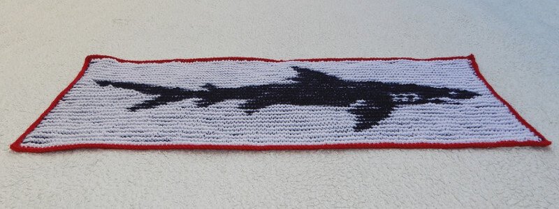 Gestrickter rechteckiger Überwurf mit schwarzem Haifisch auf weißem Hintergrund und rotem Rand