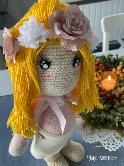 Amigurumi-Häkelpuppe mit langen gelben Garnhaaren, Blumenhaarband, großen Augen und Schleife am Hals