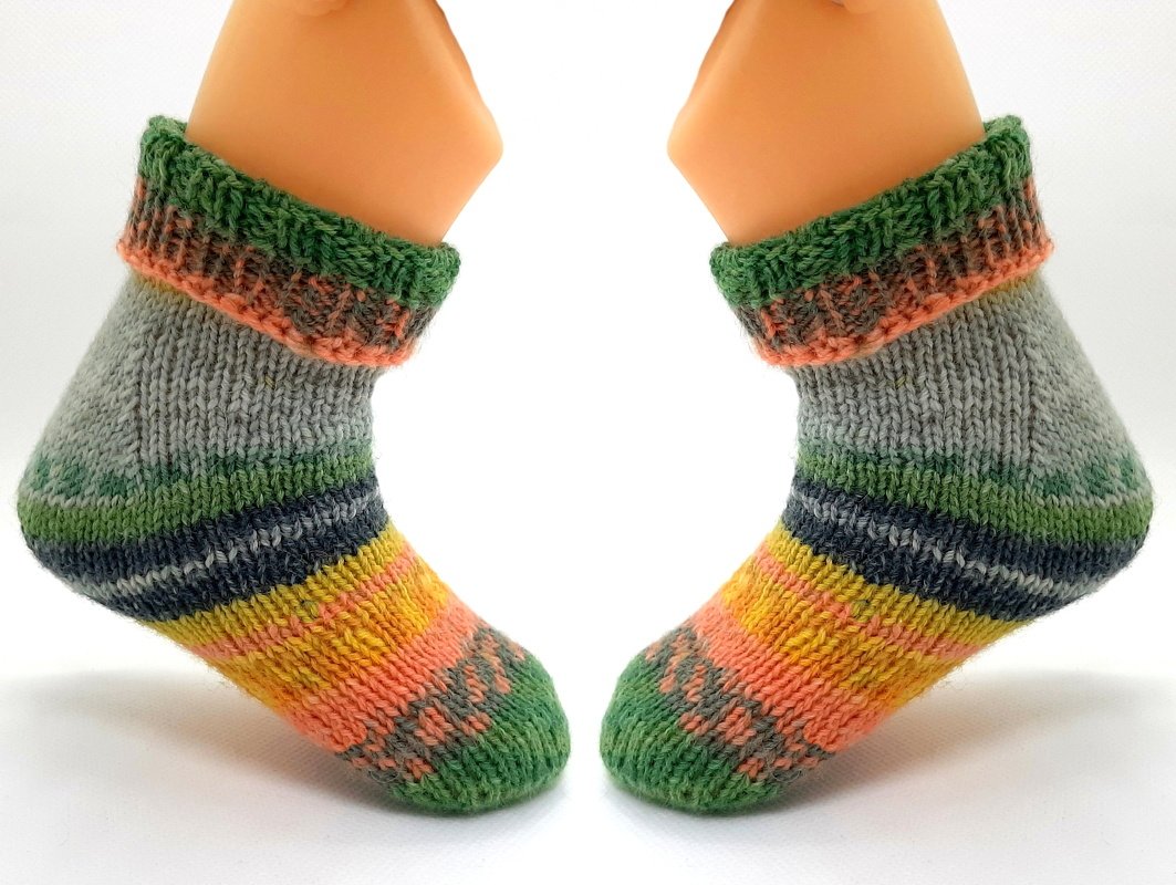 Gestrickte Babysocken mit bunten Ringelstreifen in Grün, Orange, Gelb und Grau auf Fußmodellen.