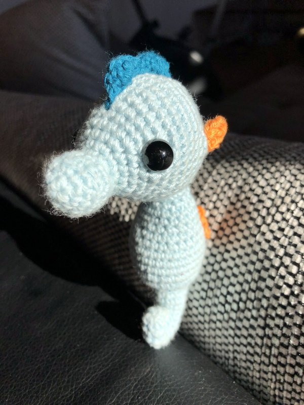Kompaktes hellblaues Amigurumi-Seepferdchen mit blauem Kamm, orangen Flossen und schwarzen Augen