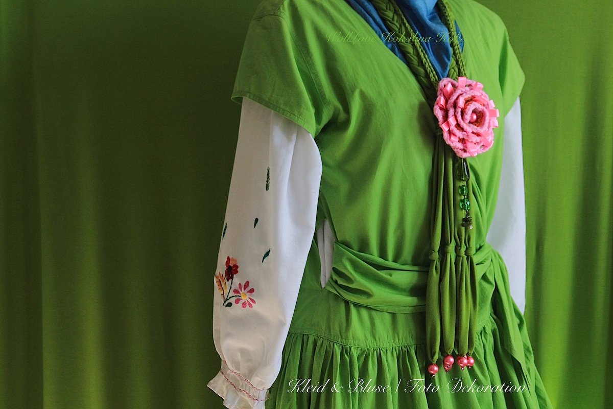 Nahaufnahme einer gehäkelten rosa Blumenkette an einem Mannequin mit grünem Kleid und bestickter weißer Bluse.