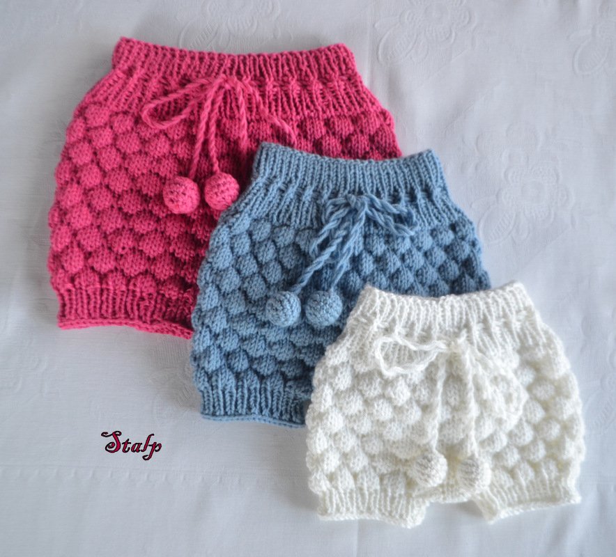 Drei gestrickte Baby-Windelhosen in Rosa, Hellblau und Weiß mit Noppenmuster, Rippenbund und Kordel mit Bommeln.