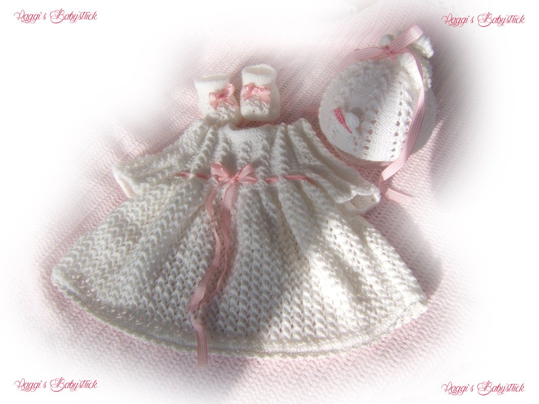 Weißes gestricktes Babykleid mit rosa Schleifen, Schühchen und Mütze auf rosa Decke