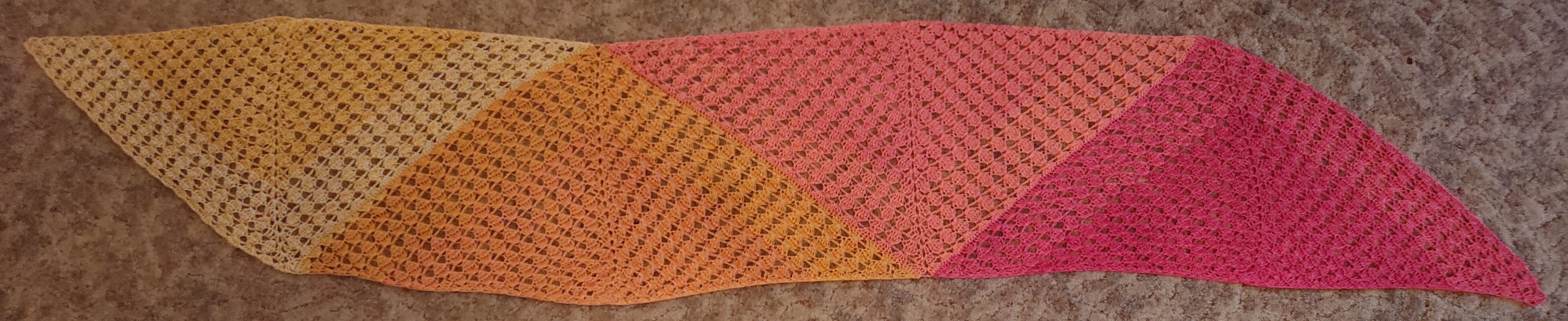 Gehäkelter Dreiecksschal mit Farbverlauf Gelb–Orange–Pink auf beigem Teppich