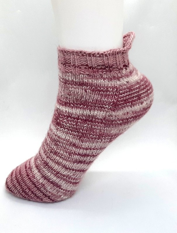 Gestrickte Kurzsocke in Beere und Creme mit Ringelmuster und kleiner Fersenlasche auf weißem Fußmodell.