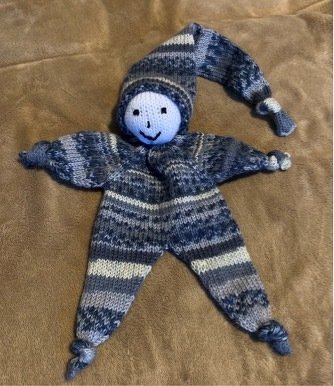 Gestrickter blaugrauer Stern-Greifling mit Gesicht und Zipfelmütze auf weichem Stoff.