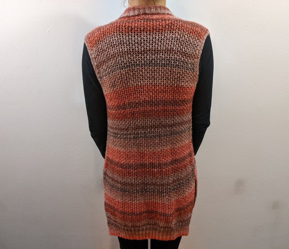 Rückenansicht einer langen Strickweste in warmen Herbsttönen über einem schwarzen Langarmshirt