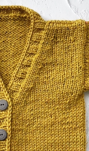 Nahaufnahme einer senfgelben, glatt rechts gestrickten Babyjacke mit V-Ausschnitt und Knöpfen
