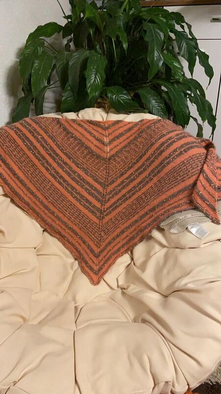 Gestricktes dreieckiges Tuch mit orange-braunen Streifen auf einem cremefarbenen Sessel