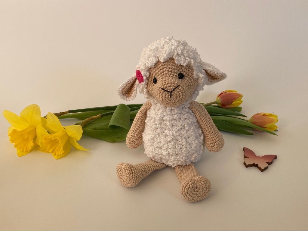 Gehäkeltes Amigurumi-Lamm mit Narzissen, Tulpen und Holzschmetterling