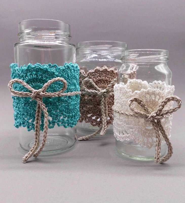 Three clear glass jars wrapped with crocheted sleeves in teal, brown, and white, each tied with a braided cord.