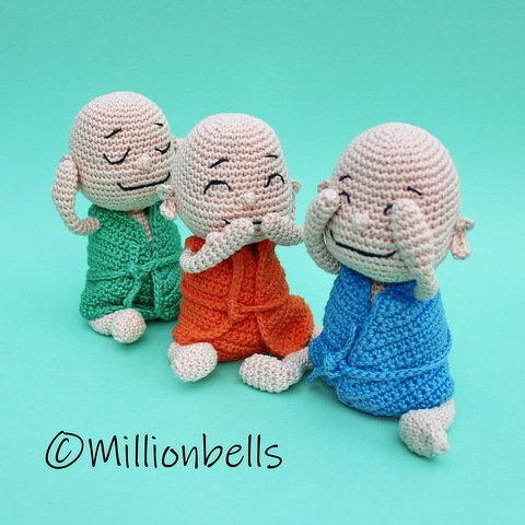 Three crocheted amigurumi figures in green, orange, and blue robes covering eyes, ears, and mouth on a teal background.