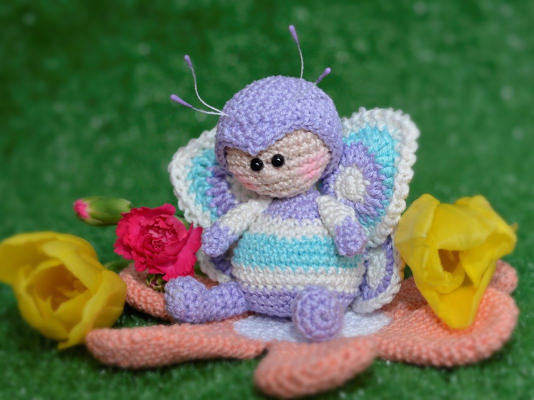 Gehäkelte pastellfarbene Schmetterlings-Amigurumi auf einer Häkelblume