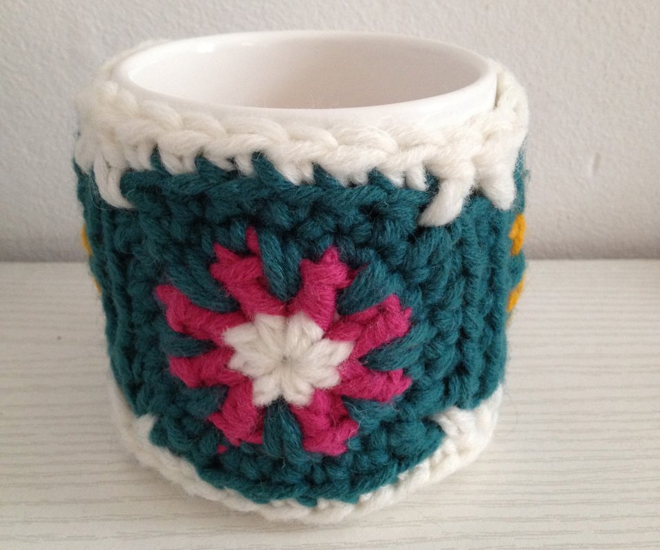Keramiktasse mit gehäkeltem Tassenwärmer im Granny‑Square‑Design in Petrol, Pink und Weiß
