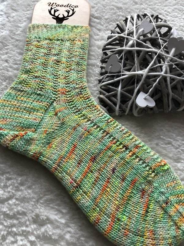 Bunte gestrickte Damensocke auf hellem, flauschigem Untergrund mit dekorativem Holzherz daneben.