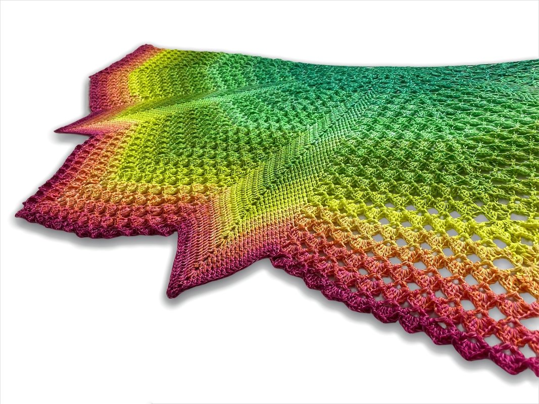 Close-up of a triangular crochet shawl in rainbow gradient yarn showing open lace mesh and pointed scalloped edges