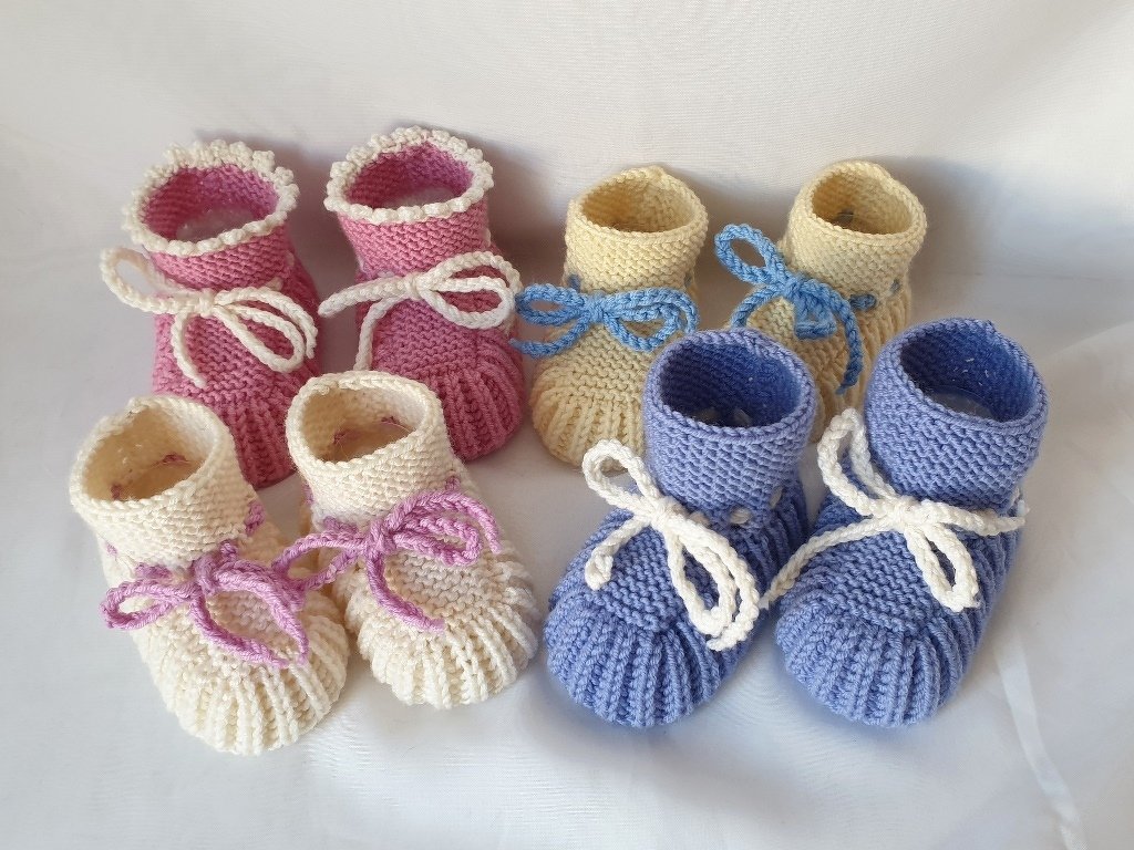 Vier Paare handgestrickter Babyschuhe in Pastell mit Schleifen auf hellem Hintergrund