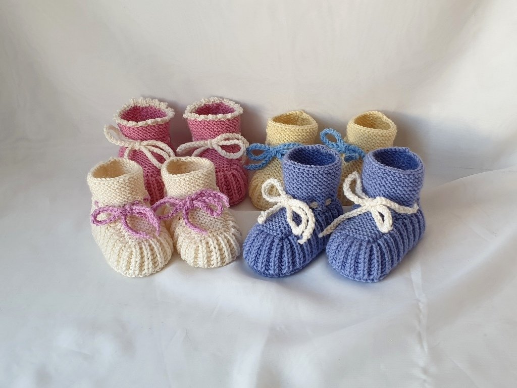 Vier handgestrickte Babyschuhe in Pastellfarben mit Bändchen