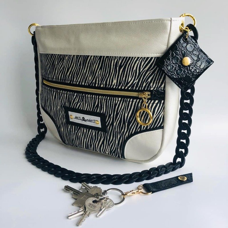 Schwarz-weiße Umhängetasche mit Zebra-Muster, schwarzem Kettenträger und goldfarbenen Details.