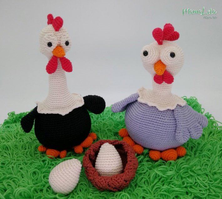 Zwei gehäkelte Hühner in Schwarz und Lila mit Nest und Eiern auf grünem Untergrund.