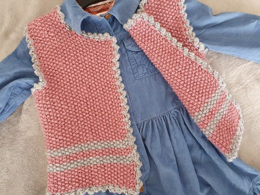 Rosa-graue gestrickte Kinderweste auf blauem Kleid