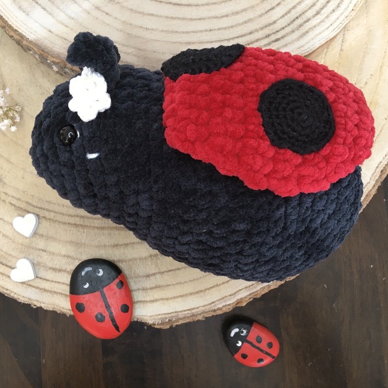 Gehäkelter Marienkäfer Amigurumi mit roten Flügeln und weißer Blüte auf Holzscheibe